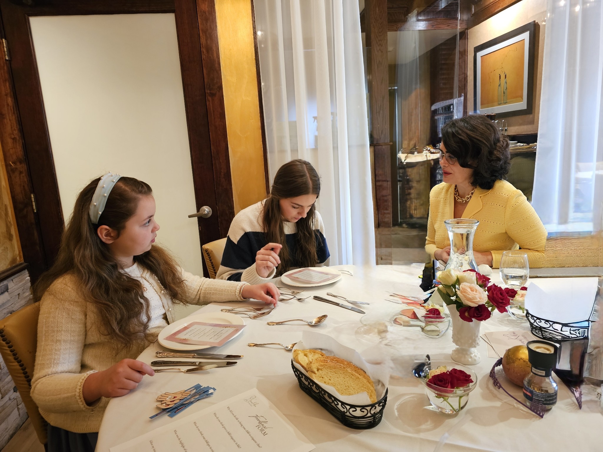Irina Khai at a laid table with two students during an etiquette workshop